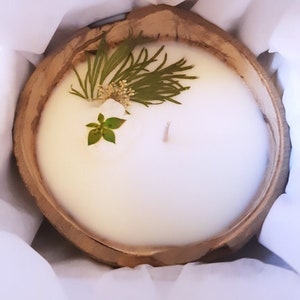 May include: A white candle with two wicks in a wooden bowl. The candle is decorated with green and white pressed flowers.