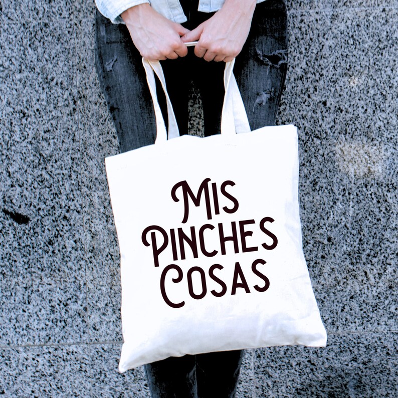May include: White tote bag with black text that reads "Mis Pinches Cosas".