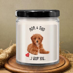 May include: A white candle jar with a black lid. The label features a red and white heart balloon, a brown puppy, and the text "Mom & Dad... I woof you..."