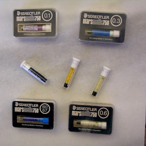Op de afbeelding: Een verzameling Staedtler Marsmatic 750 technische penvullingen in verschillende maten, waaronder 0,1, 0,3, 0,6 en 0,7. Elke vulling zit in een transparante plastic verpakking met het Staedtler-logo en "Nürnberg Made in Germany".