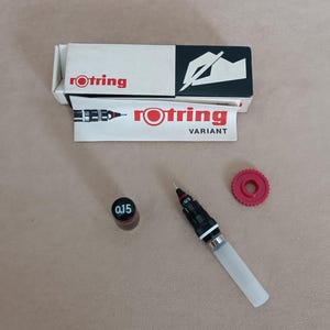 Op de afbeelding: Een rode en zwarte Rotring Variant pen met een zwart-witte 0,15 mm punt en een rode dop. De pen ligt op een beige oppervlak met een rode plastic dop en een doos met het Rotring-logo.