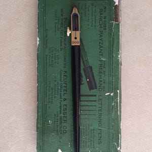 Könnte beinhalten: Ein schwarzer und goldener Schriftzugstift mit der Nummer "000" darauf, der auf einer grünen Box liegt. Auf der Box steht "BARCH-PAYZANT FREEHAND LETTERING PENS" und "SOLE MANUFACTURERS KEUFFEL & ESSER CO."
