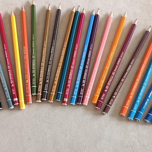May include: A collection of colored pencils in various shades, including blue, orange, green, and red. Each pencil has a wooden body and a sharpened graphite tip. The pencils are arranged in a semi-circular pattern.