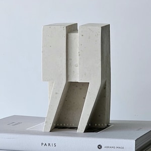 Könnte beinhalten: Eine weiße Betonskulptur eines Gebäudes mit geometrischem Design, die auf einem Stapel Bücher steht. Die Bücher tragen Titel wie "Paris", "The Creative Act" und "Rick Rubin".