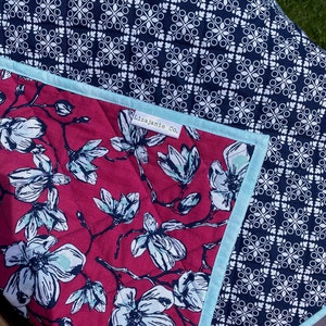 May include: A red and white floral quilt with a blue and white geometric pattern on the back. The quilt has a blue binding and a label that reads "Lizajanie Co."