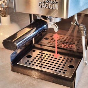 Könnte beinhalten: Nahaufnahme einer Gaggia Classic Espressomaschine. Die Maschine ist aus Edelstahl mit einem schwarzen Griff und einer Abtropfschale. Die Abtropfschale ist etwa 10 cm vom Siebträger entfernt. Das Wort "Gaggia" ist oben zu sehen.