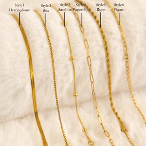 May include: Six gold necklaces are displayed, each with a different chain design. Styles include herringbone, box, satellite, paperclip, rope, and figaro. The necklaces are shown on a soft, white surface.