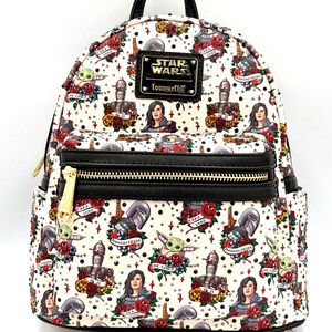 May include: A white mini backpack featuring a repeating tattoo-style print of Star Wars characters including The Child, Cara Dune, IG-11, and The Mandalorian surrounded by red roses. It has a black top handle, black trim, and a gold Star Wars Loungefly logo.