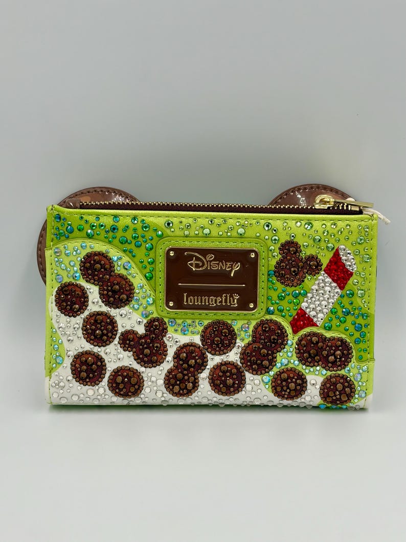 May include: A lime green Disney Loungefly wallet with brown Mickey Mouse ear accents. The wallet features brown, white, and red embellishments, including Mickey Mouse shapes and a candy cane design. The Disney and Loungefly logos are visible.