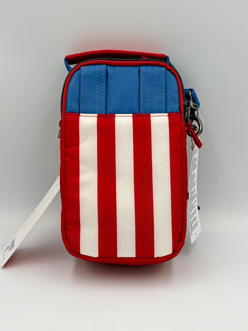 May include: A rectangular crossbody bag featuring a vertical striped pattern of red and white on the lower section and a solid blue panel on the upper section. The bag includes a top handle, a zipper closure, and a metal clip attachment on the side.