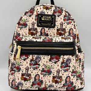 May include: Cream-coloured Star Wars Loungefly mini backpack with a black top handle and trim. The backpack features a repeating tattoo-style print of characters like The Child, Cara Dune, and the Mandalorian, with red roses and stars.