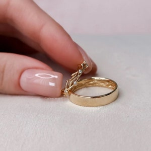 May include: Two gold wedding bands, one with a delicate vine design and small diamonds, the other a simple band.