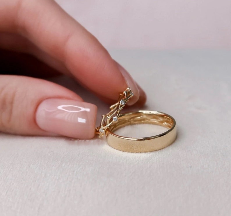 May include: Two gold wedding bands, one with a delicate vine design and small diamonds, the other a simple band.