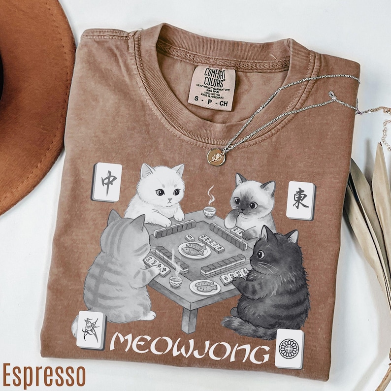 a brown t-shirt with a graphic design depicting four cats playing a game of mahjong.
