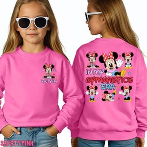 A young girl wearing a pink sweatshirt with Minnie Mouse characters and text on the back.