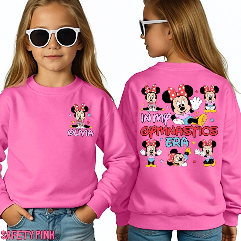 A young girl wearing a pink sweatshirt with Minnie Mouse characters and text on the back.
