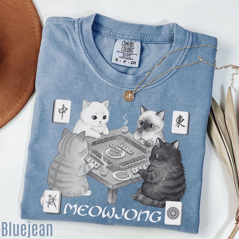 A blue t-shirt with a cat-themed graphic design, featuring a cat playing a game of Meowwong with two other cats.
