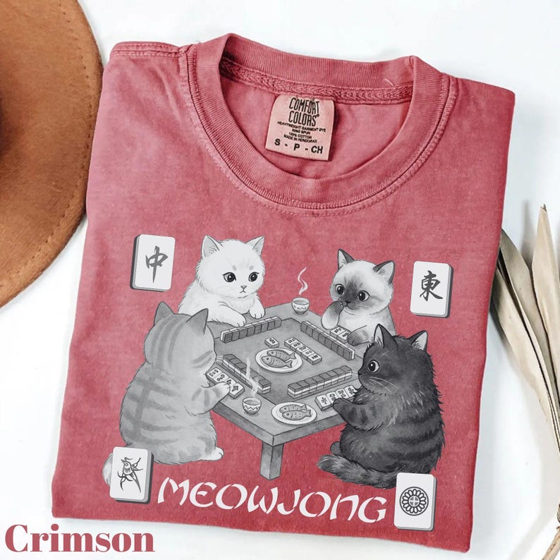 a red t-shirt with a graphic design depicting three cats playing a game of Meowwong, a popular Chinese card game.