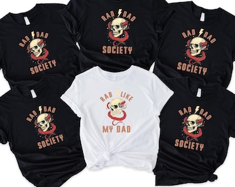 May include: Black and white t-shirts with a skull graphic and the words "RAD DAD SOCIETY". One white t-shirt features the text "RAD LIKE MY DAD". The skull design includes a red snake and lightning bolt.