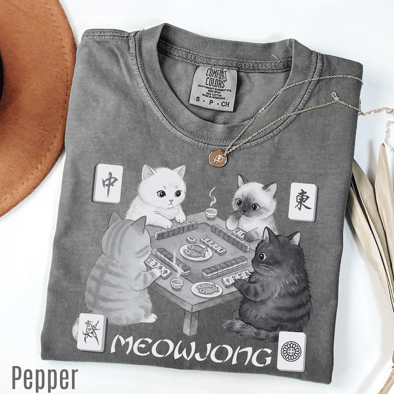 a gray t-shirt with a graphic design depicting four cats playing a game of Meowwong, a popular Chinese card game.