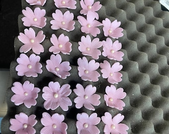 May include: A collection of 30 pale pink sugar flowers with white pearl centers arranged on a gray foam surface.