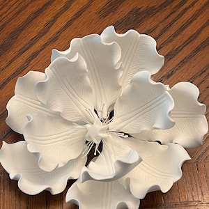 May include: A white ceramic flower with ruffled petals. The flower is made of a smooth, white material and has a delicate, feminine look.