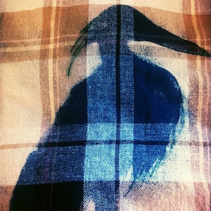 May include: A blue silhouette of a bird on a plaid fabric background. The fabric is a mix of brown, white, and beige.