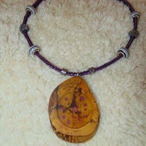 May include: A purple and black braided cord necklace with silver beads and a wooden pendant with purple accents.
