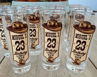 May include: A set of clear glass shot glasses featuring a brown graphic of a cowboy hat, a pair of boots, and the text "MIGUEL'S 23 Birthday PARTY 03.07.26". Each glass has a cylindrical shape and displays the same western-themed design in brown ink.