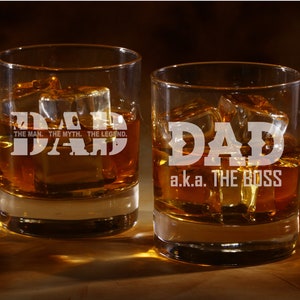 May include: Two clear glass tumblers with the word "DAD" etched on them. One tumbler says "DAD, THE MAN, THE MYTH, THE LEGEND." The other tumbler says "DAD a.k.a. THE BOSS". Both tumblers are filled with amber liquid and ice cubes.