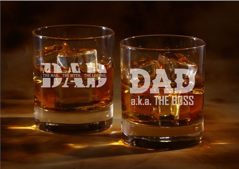 May include: Two clear glass tumblers with the word "DAD" etched on them. One tumbler says "DAD, THE MAN, THE MYTH, THE LEGEND." The other tumbler says "DAD a.k.a. THE BOSS". Both tumblers are filled with amber liquid and ice cubes.