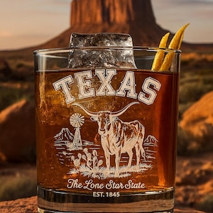 May include: A rocks glass filled with a brown liquid, ice, and a lemon peel garnish. The glass features the word "TEXAS" and an illustration of a longhorn, windmill, and cactus. The words "The Lone Star State" and "EST. 1845" are also visible.