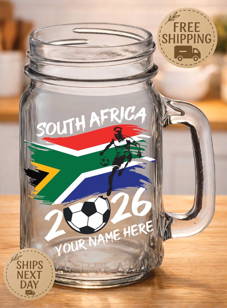 May include: Clear glass mason jar with a handle, featuring a South African flag design and a soccer player graphic. The text "SOUTH AFRICA 2026" and "YOUR NAME HERE" are also displayed. Includes a soccer ball graphic.