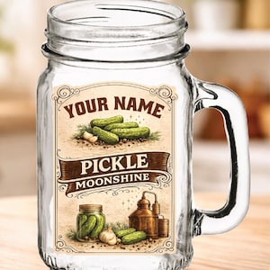 May include: Clear glass mason jar with a handle, featuring a label that reads "YOUR NAME PICKLE MOONSHINE." The label includes illustrations of pickles, garlic, and a still. The jar is designed for beverages.