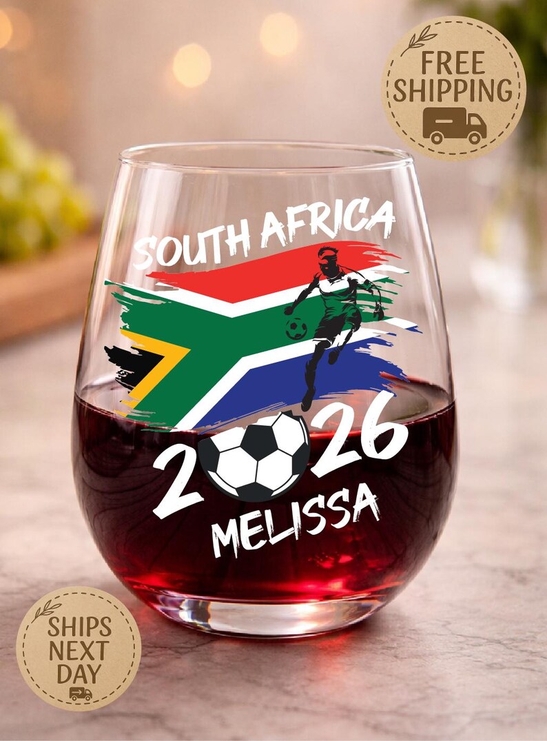 May include: Stemless wine glass filled with red liquid, featuring a South Africa flag design, a soccer player graphic, and the text "SOUTH AFRICA 2026 MELISSA". The glass has a soccer ball graphic.