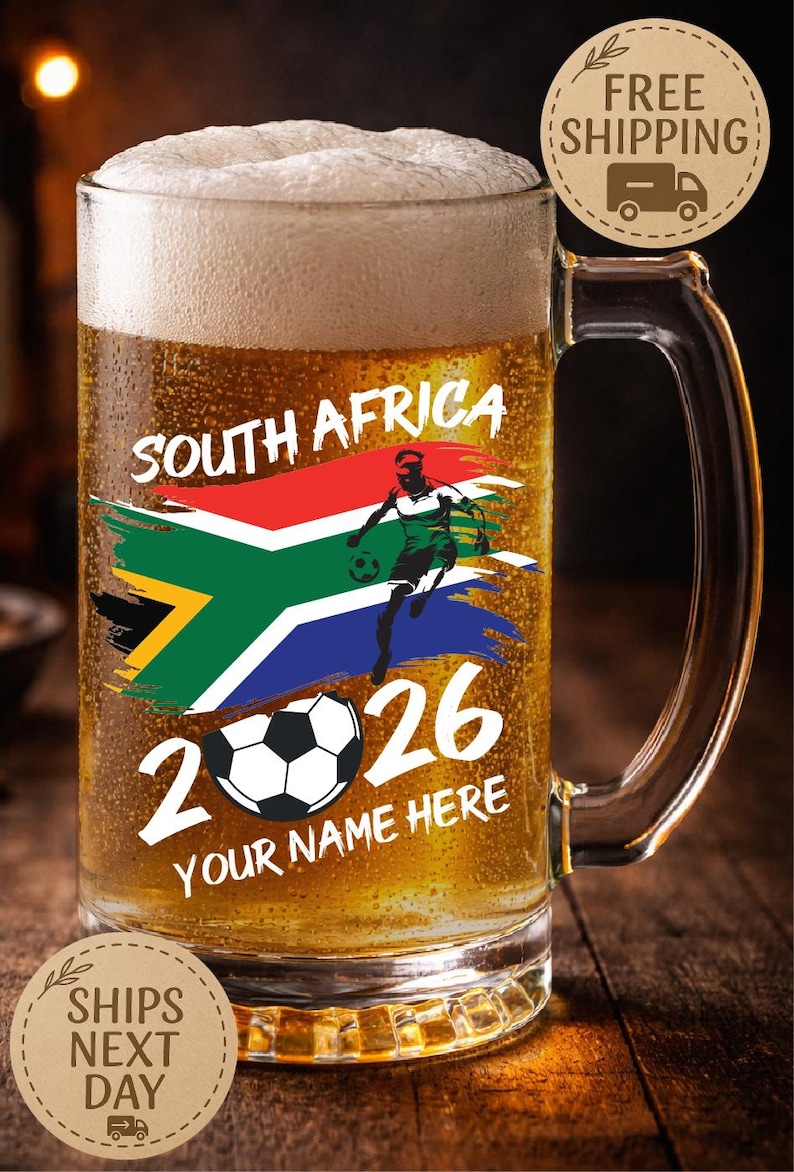 May include: A clear glass beer mug filled with beer and foam. The mug features the South African flag, a soccer player graphic, the numbers "2026", and the text "YOUR NAME HERE".