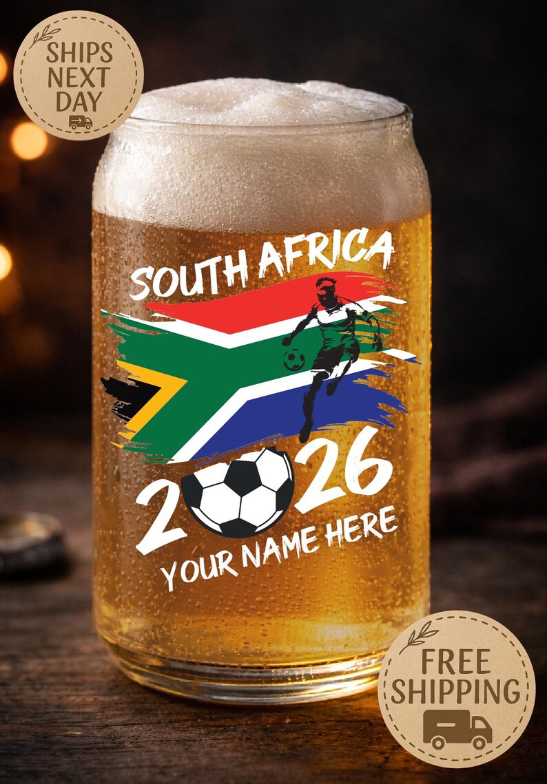 May include: A glass of beer with a design featuring the South African flag, a soccer player, and the text "SOUTH AFRICA 2026". The words "YOUR NAME HERE" are also included. The glass is filled with beer and has condensation.