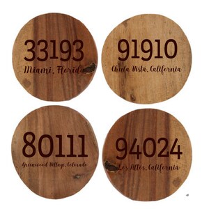 May include: Four round wooden coasters with engraved text. Each coaster displays a different zip code and city: 33193 Miami, Florida; 91910 Chula Vista, California; 80111 Greenwood Village, Colorado; and 94024 Los Altos, California.
