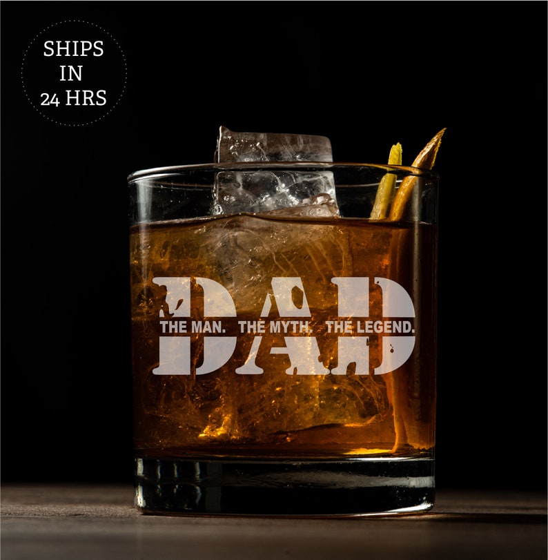 May include: A clear glass with a brown liquid and ice cubes. The glass has the words "DAD THE MAN. THE MYTH. THE LEGEND." etched on the side.