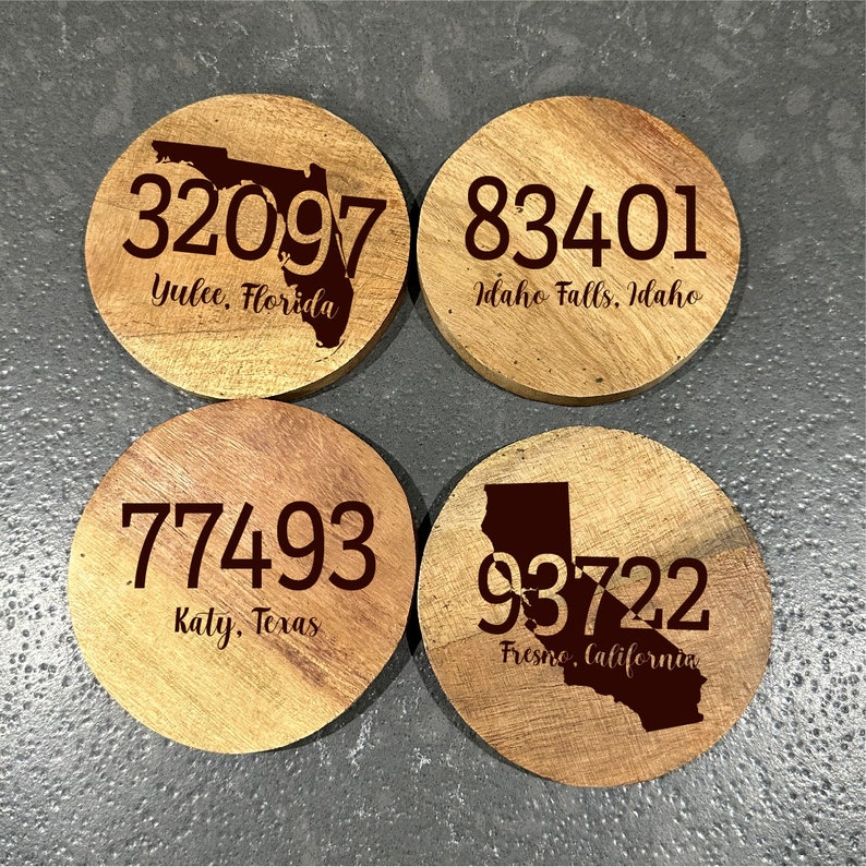 May include: Four round wooden coasters with engraved text and state outlines. Each coaster features a different zip code and city: 32097 Yulee, Florida; 83401 Idaho Falls, Idaho; 77493 Katy, Texas; and 93722 Fresno, California.