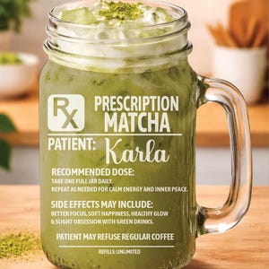 May include: A clear glass mason jar filled with green matcha drink, ice, and matcha powder on top. The jar has a handle and text that reads "Prescription Matcha" and "Patient: Karla". The drink is on a wooden surface.