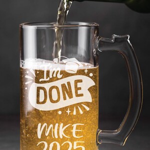 May include: A clear glass beer mug with a handle, filled with a golden liquid. The mug has the text "I'm Done" with a graduation cap above the text, and "Mike 2025" below the text.