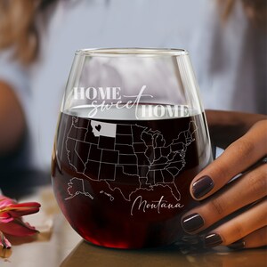 May include: A stemless wine glass filled with red wine, etched with a map of the United States, highlighting Montana. The words "HOME sweet HOME" are displayed, along with the name "Montana".
