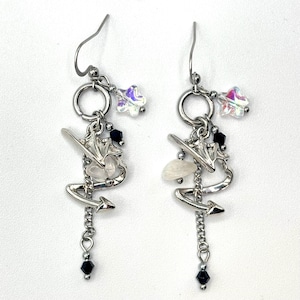May include: Silver dangle earrings with multiple charms, including a star, a small white shell, a black bead, and a silver charm that resembles a bird or a bat.