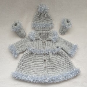 May include: A grey knitted baby coat with a silver trim, matching hat and booties. The coat has a button fastening and a hood.