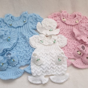 May include: Three knitted baby outfits, one blue, one pink and one white. Each outfit includes a dress, hat and booties.