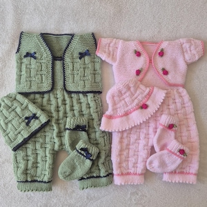 以下が含まれることがあります： 2つのニットベビー服セット。1つは、ダークブルーのトリムとリボンが付いた、お揃いの帽子、ベスト、パンツ、靴下が付いたライトグリーンです。もう1つは、ピンクのトリムとバラのアクセントが付いた、お揃いの帽子、カーディガン、パンツ、靴下が付いたピンクです。
