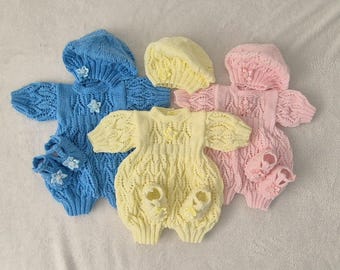 May include: Three knitted baby outfits in blue, yellow and pink. Each outfit includes a matching hat and booties. The outfits are made with a delicate cable knit pattern and feature flower embellishments.