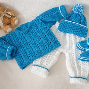 May include: A knitted baby outfit set in blue and white. The set includes a sweater, trousers, hat, and booties. The sweater and hat are blue with white trim, while the trousers and booties are white with blue trim.
