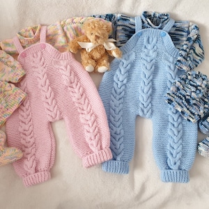 May include: Two knitted baby outfits, one pink and one blue, with matching hats. The outfits are cable knit and have a button closure. The hats are also cable knit and have a pom-pom on top.